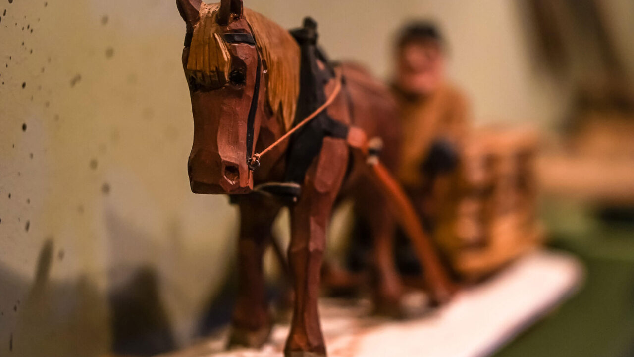 A horse carved in a tree. The horse's head is in focus, but it can be guessed that it is a sled with a person behind.