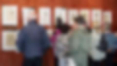 A group of people are looking at paintings hanging on a red wall. The paintings are portraits drawn in pencil.