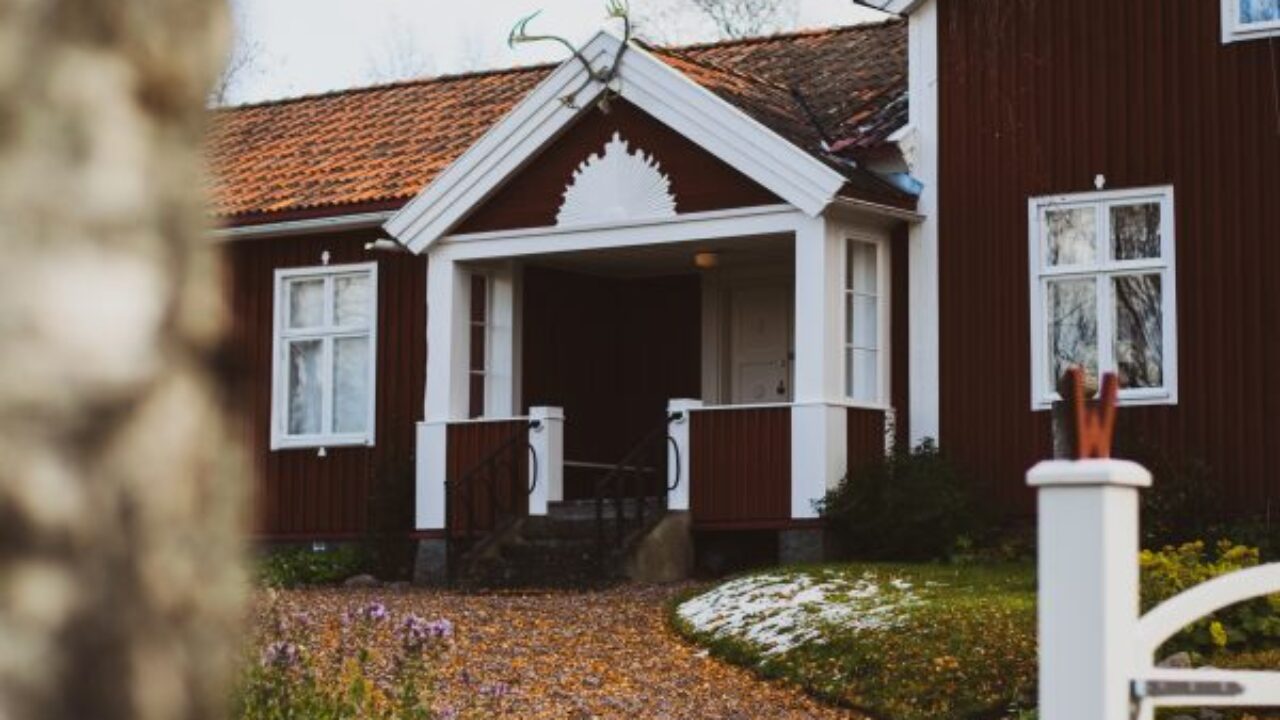 Red house with white details. On the roof ridge is a reindeer horn. Gravel path up to the house which has been covered with orange fall leaves.