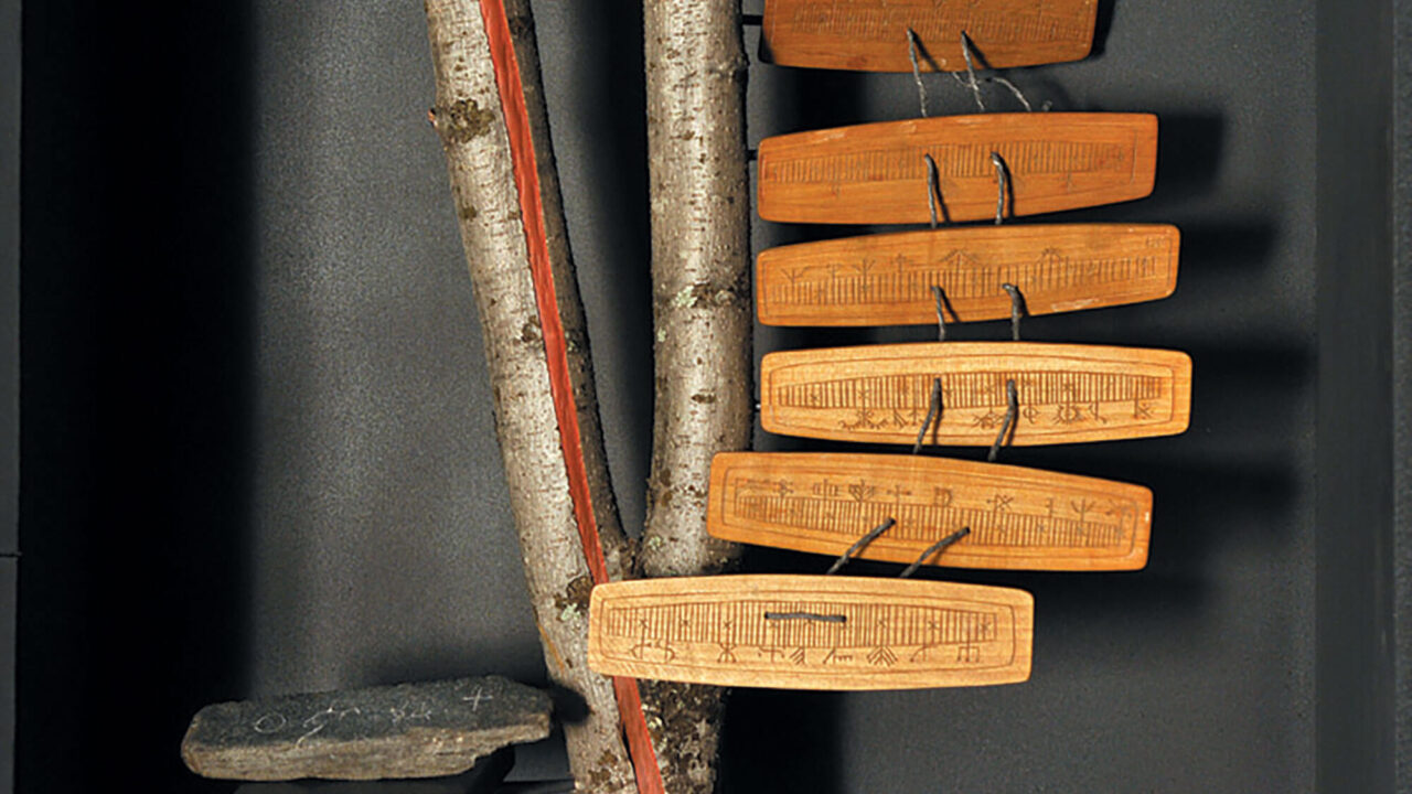 Ur Silvermuseets utställning Ur naturen: en träkalender bestående av sex träskivor med inristade streck och symboler. Kalendern hänger på en trädstam.