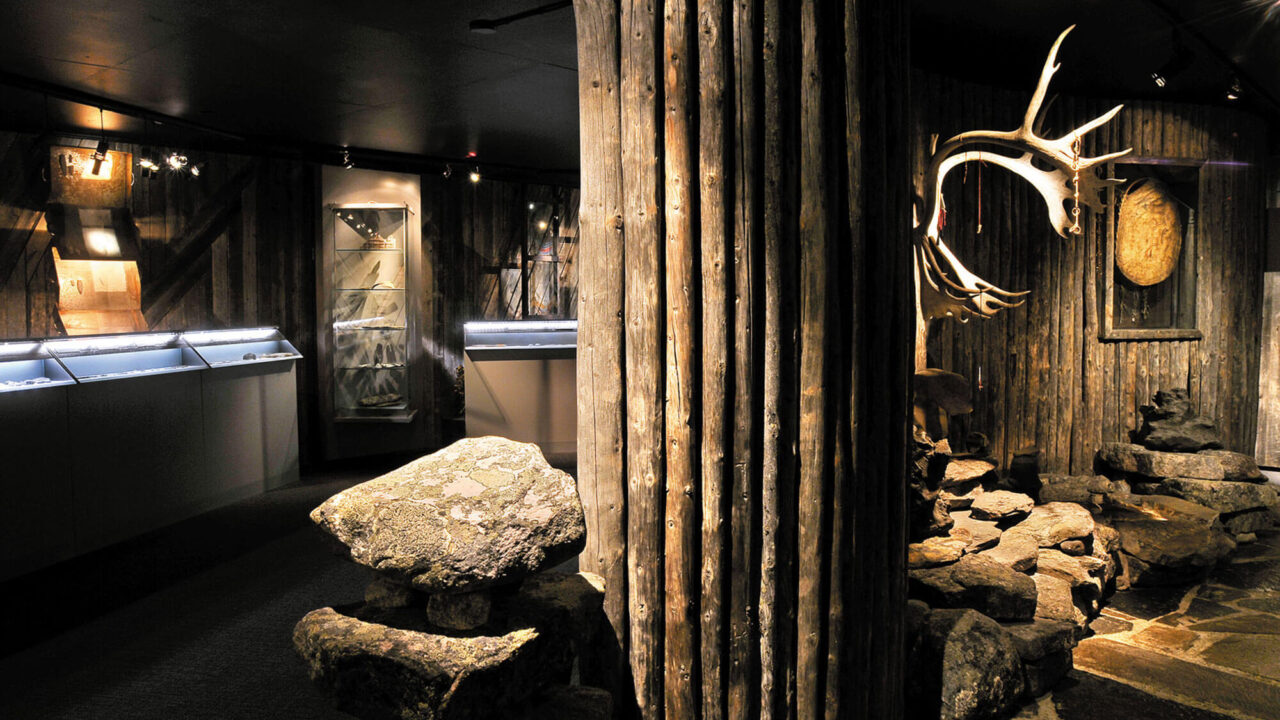 View of the exhibition Traces. Gray wood, stone and stands. In one stand we see a drum.