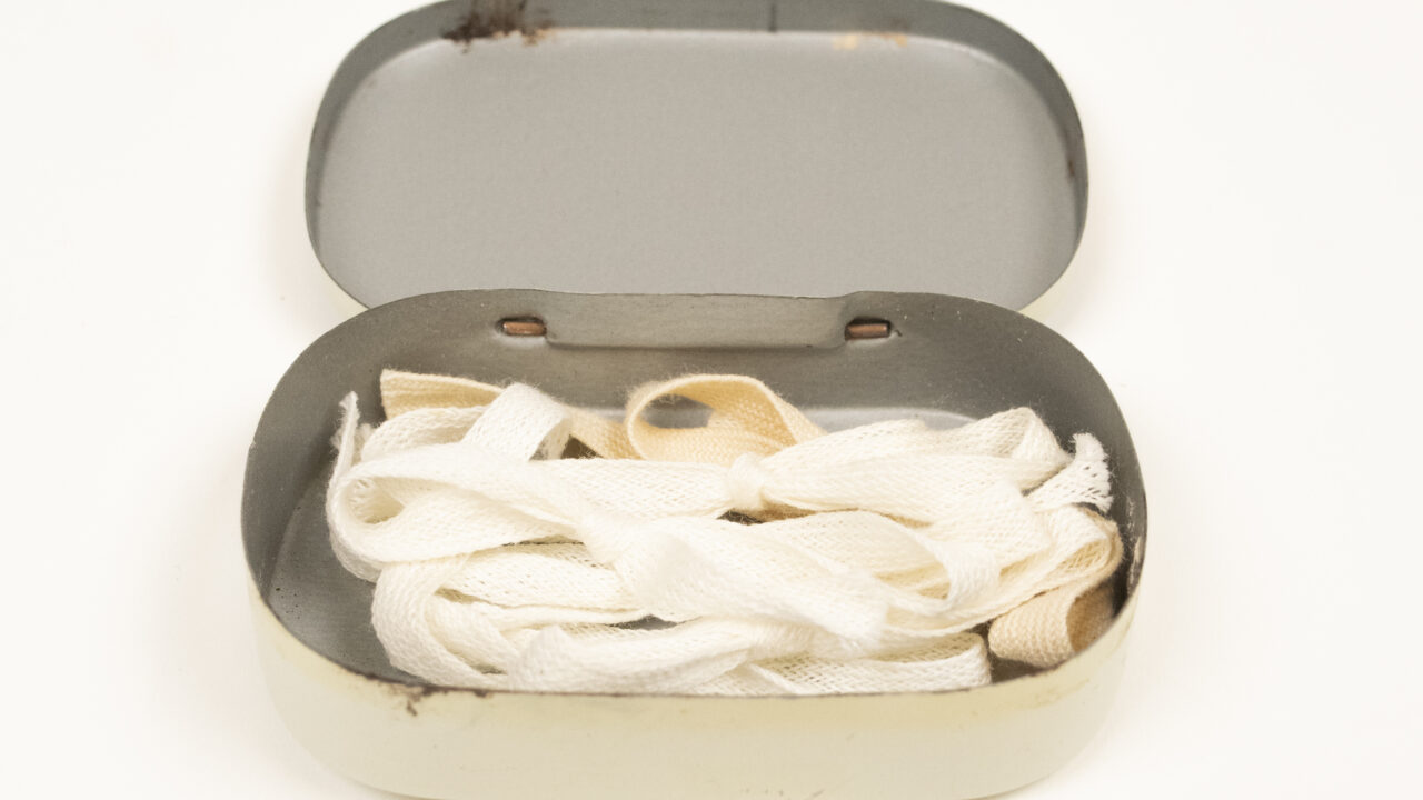 Small medicine box with open lid, small ribbons are inside.