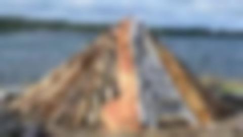 Resverk till en kåta där det har påbörjats näverläggning. I bakgrunden vatten och en mörkblå molnig himmel.