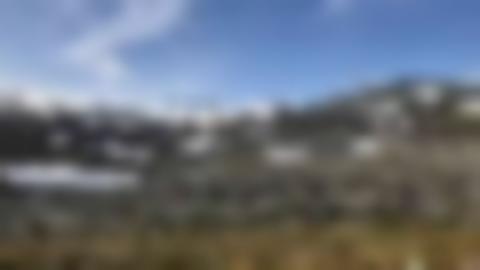 Gråaktig högfjällsmiljö med mycket sten, toppar och snöfläckar. I mitten rinner en bäck.