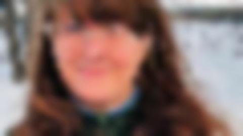 Porträtt av Ingela Edholm som har brunt axellångt hår, glasögon och en grön tröja. Hon ler lite och kisar in i kameran,