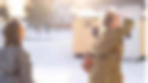 Två sagofigurer (utklädda personer) spejar mot något utanför bild. Backen är snötäckt och solen skiner.