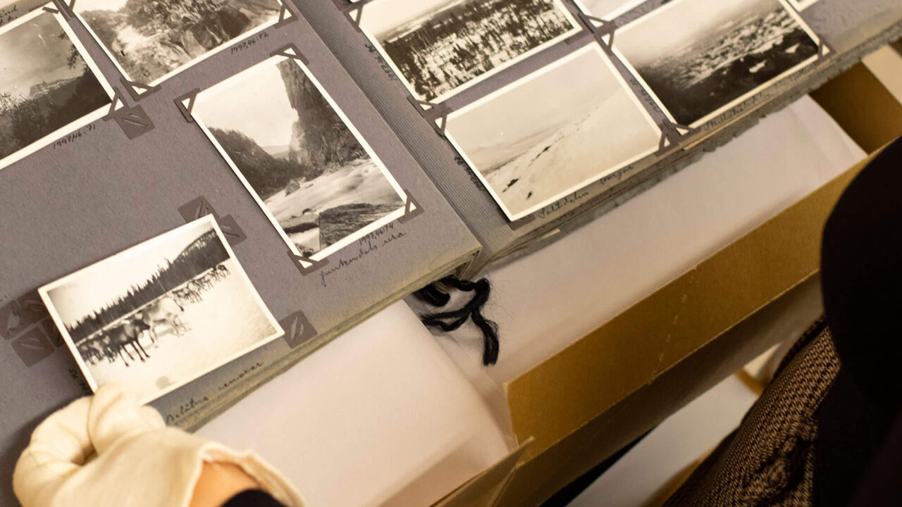 Någon bläddrar i ett gammalt fotoalbum med svartvita foton. Personens ena hand med vit tyghandske syns.