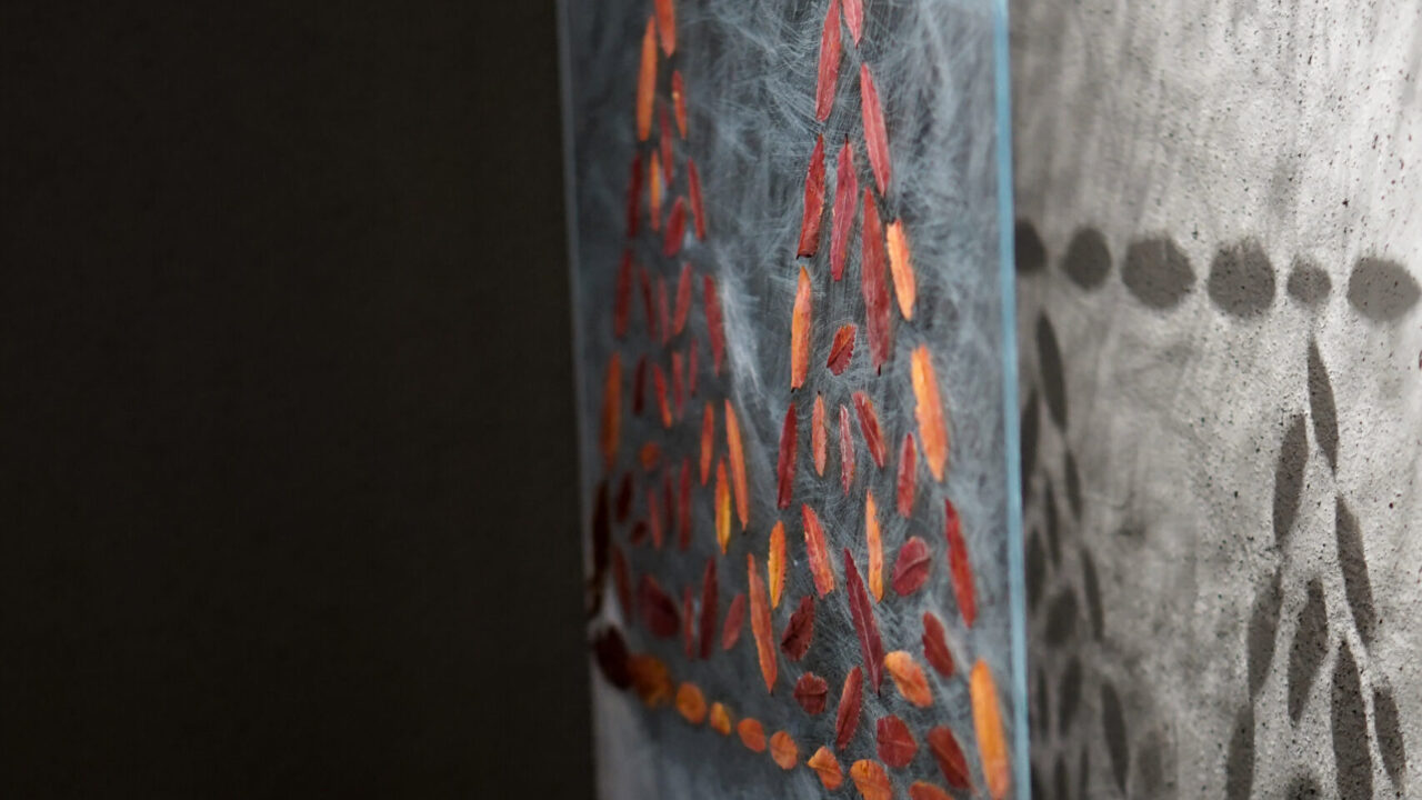 Plexiglas panel with glued red leaves forming a zigzag pattern. The pattern shadows the wall behind.