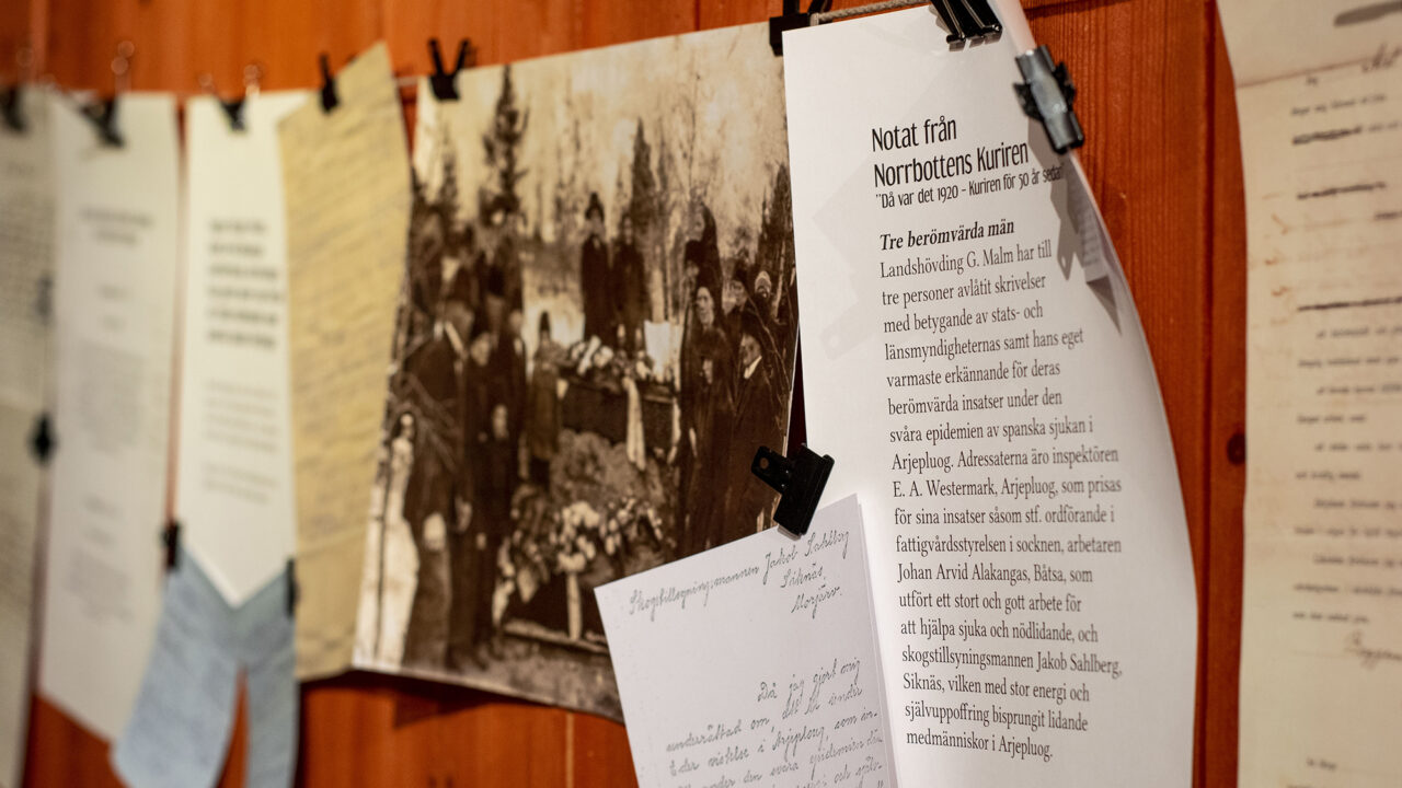 Image of posters and pictures hanging on a rope with a rust-red wall behind.