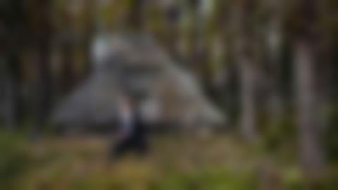 Mansperson i svarta kläder sitter på bron till en timrad kåta