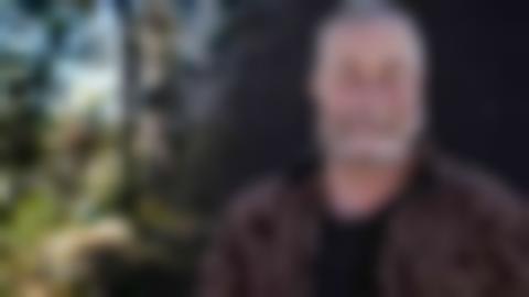 En bild som visar en skog. Ett porträtt av en gråhårig man har lagts ovanpå skogsbilden.