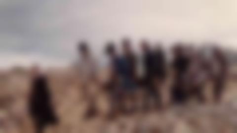 I en karg fjällmiljö går en person i svart kappa framför ett följe på 8-10 personer som bär en likkista,