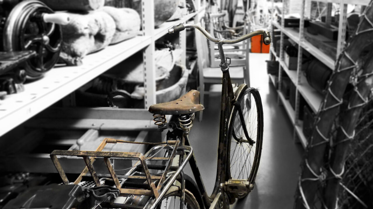 En gammal cykel står i ett magasin med många gamla saker.