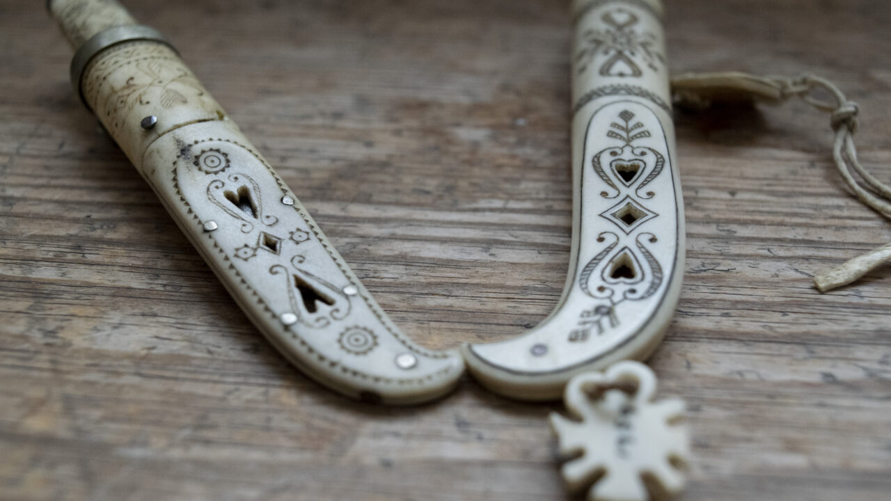 Två helhornsknivar ligger bredvid varandra. Slidorna är genomhålade med hjärtan och graverade.