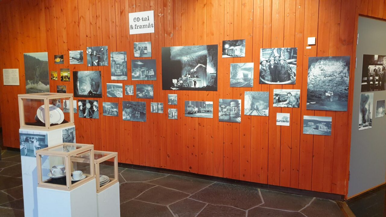 Parti ur utställningen Länge leve Laisvall. Svartvita fotografier på roströd vägg, montrar med porslin
